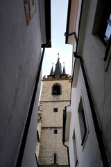 View of historic church tower framed by narrow alley walls, symbolizing medieval architecture, cultural heritage, spiritual presence, and timeless urban scenery.