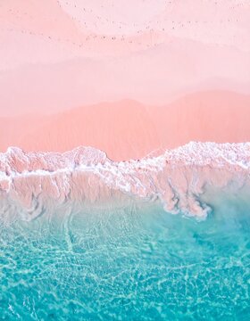 An aerial shot of a stunning pink sand beach meeting crystal clear turquoise waters, with gentle waves lapping the shore