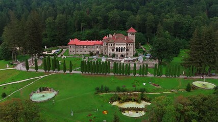 Rising over the meadow in front of the famous Cantacuzino Castle. Pine tree wood growing on the mountain slope at backdrop. Busteni, Romania.