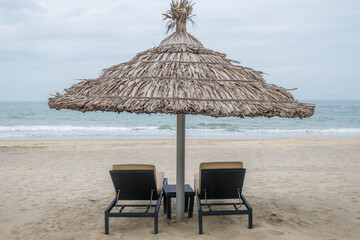 Pair of deck chairs under a palm umbrella in beautiful Cua Dai Beach in Hoi An, Central Vietnam