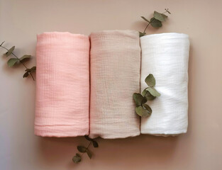 Soft muslin blankets in pastel colors rolled and stacked with eucalyptus leaves