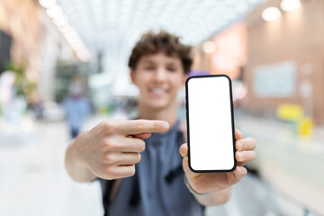 Young Caucasian man at airport holding smartphone close up with blank white screen. Concept for mockup, digital travel tools, technology, and modern youth