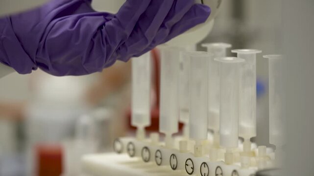 Close-up detailed view of a woman in lab wear carefully pouring equal small volumes of solvent from one bottle into multiple flasks &mdash;  themes of precision, accuracy, science, chemistry, method.