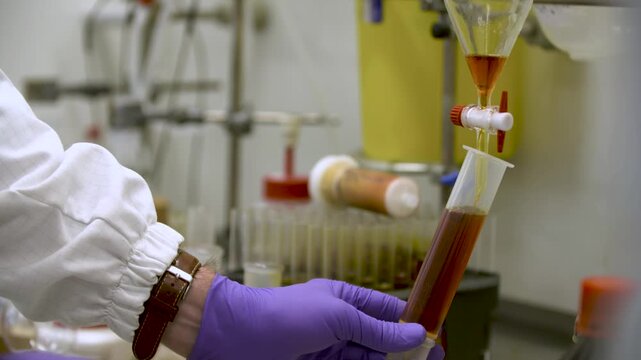 Close-up detailed view of a woman in laboratory gloves carefully releasing orange liquid from a burette tap into a smaller container &mdash; perfect for themes of science, chemistry, precision, and analysis
