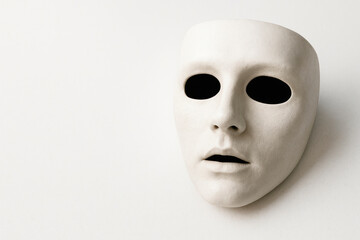 A white mask with empty eye sockets on a light background. Space for text.