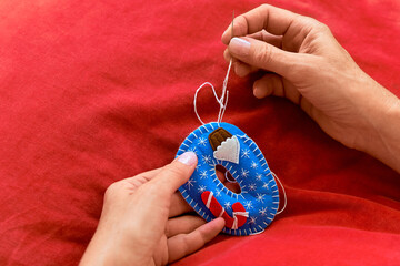 Hands sewing handmade felt Christmas ornament with needle and thread. DIY festive craft decoration...