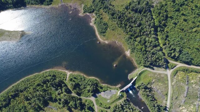 Aerial view at over 500m altitude on the Mitis Dam at the outlet of Lake Mitis where a renowned salmon river flows through the woods and the lush forest, Quebec, Canada, 2025.