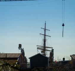 Tall ship mast and rigging behind harbor buildings.