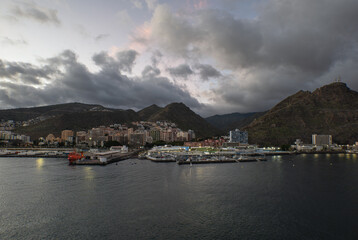 Early morning view of Tenerife with harbor, city scape, and dramatic mountain backdrop under soft sunlight and scattered clouds.