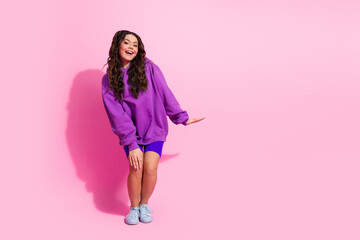 Young female athlete posing joyfully in a trendy purple sweatshirt on a pink backdrop