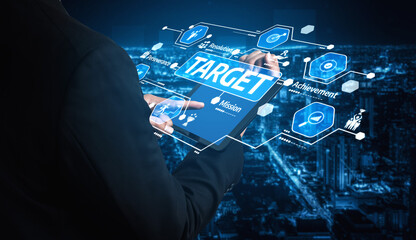 A businessman interacts with a futuristic tablet displaying target setting and strategic icons, emphasizing achievement and planning in a vibrant urban setting. Tessel