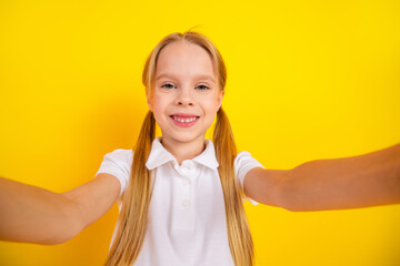 Cheerful schoolgirl taking a selfie against a vibrant yellow background, expressing joy and energy,...