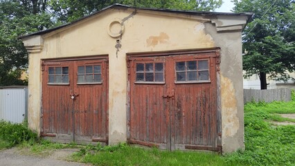 Rustic weathered barn with two large wooden doors and windows, set against backdrop of lush greenery. Peeling paint and aged wood add character to this charming rural structure