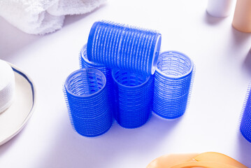 Set of Blue Plastic Hair Rollers with Hair Care Products on White Table