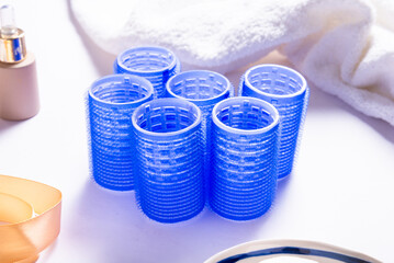 Set of Blue Plastic Hair Rollers with Hair Care Products on White Table