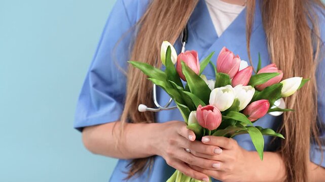Portrait of a young Caucasian female doctor in a blue uniform on an isolated background with flowers. Good for a pediatrician or gynecologist. Doctors' Day, Medical Worker's Day