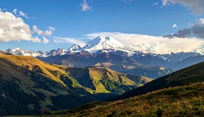 Obraz premium A breathtaking vista of snow-capped mountains, bathed in golden sunlight, with rolling hills and valleys of varying shades of green and brown.