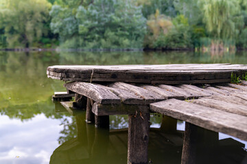 Wooden pier on calm lake with green trees reflection. Outdoor landscape photography. Nature travel and relaxation concept. Design for poster, wallpaper, banner, postcard, greeting card, invitation.