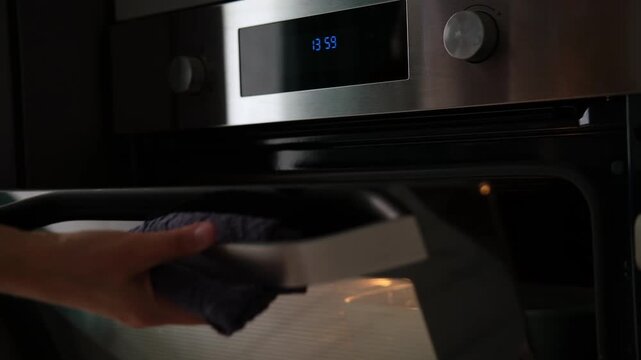 Side view of the woman turning on the electrical oven in the kitchen to baking dessert. Checking readiness of the food