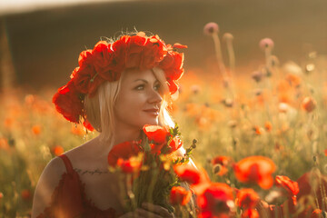 A woman wearing a red flower crown stands in a field of red flowers