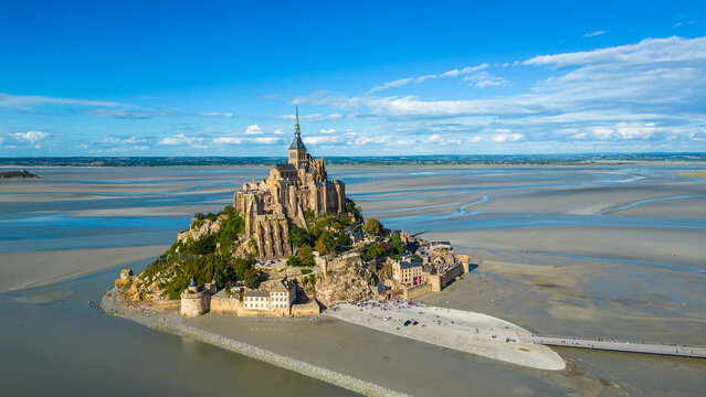 Aerial view of Mont Saint Michel in Normandy, France, during low tide, showing the iconic abbey rising above the sandy bay, a UNESCO World Heritage site and popular tourist destination