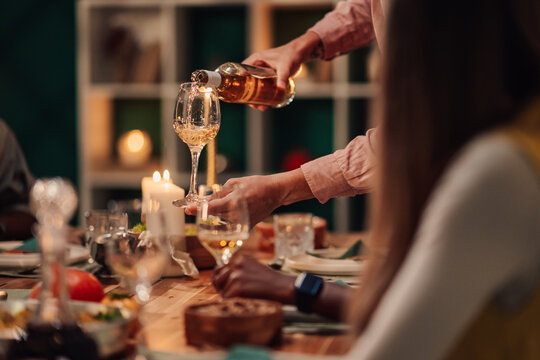 Waiter pouring white wine into glass at dinner party with friends
