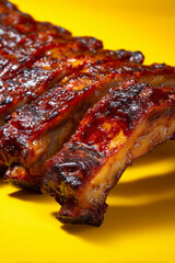 Grilled delicious barbecue ribs with crispy crust close up detail against vibrant yellow background.