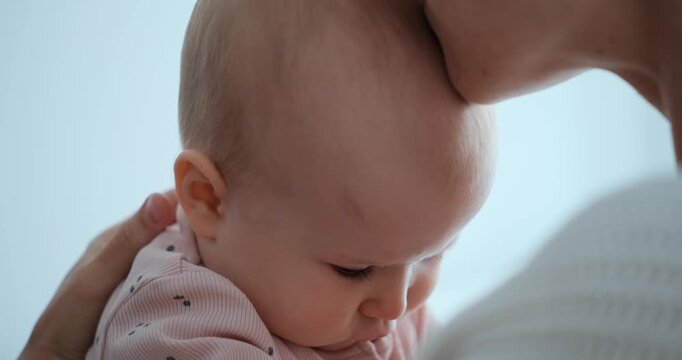 Slow-motion closeup of a mother kissing her infant daughters forehead while gently holding her.