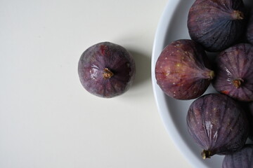 Fresh purple fig with a bowl of ripe figs on a white background. Healthy seasonal fruit rich in vitamins and nutrients, perfect for cookbooks, blogs, and healthy lifestyle content.