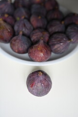 Top view of fresh purple figs on white plate with one fig aside. Nutritious superfood rich in vitamins and antioxidants, ideal for fitness nutrition, diet blogs and wellness concepts.