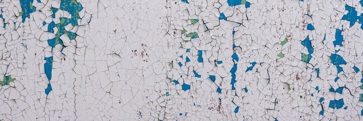 Fototapeta premium Peeling paint on the wall. Panorama of a concrete wall with old cracked flaking paint. Weathered rough painted surface with patterns of cracks and peeling. Wide panoramic texture for grunge background