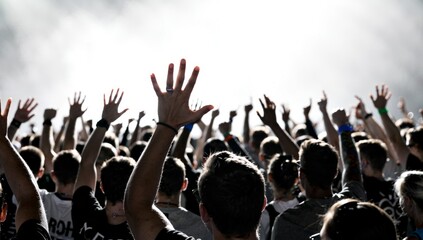 Photograph of energetic concert crowd with raised hands, low-angle perspective emphasizing scale and excitement, high contrast silhouettes against bright background, collective