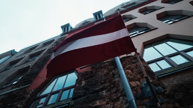 The Latvian flag proudly waves above a historic building set within a vibrant urban environment, showcasing heritage