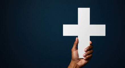 Obraz premium African american hand holding a white christian cross against a solid dark background. Concept of faith, baptism, and spiritual devotion.