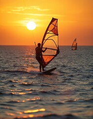 Man windsurfs on ocean at sunset. Golden sun shines brightly in orange sky. Person rides board on water creating splash. Sport activity, adventure, freedom. Another windsurfer far away. Summer trip