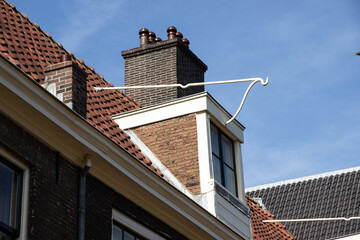 Architectural detail of a traditional building featuring a chimney, sloped roof, and clear blue sky, showcasing unique design elements and craftsmanship in urban.