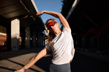 Athletic woman stretching outdoors wearing sunglasses during morning workout