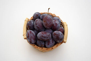 Plums in a small basket, white background. Fresh organic fruit