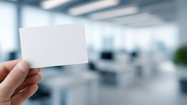 Blank business card held by hand in modern office environment with blurred background, conveying professionalism and opportunity