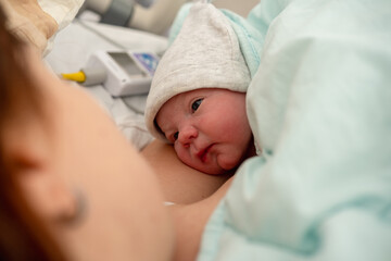 Newborn baby wearing a cozy hat, resting peacefully on mother's chest in a hospital room, enjoying...