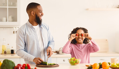 Kitchen Fun. Portrait of funny black little girl playing with food, pretending tomatoes vegetables...