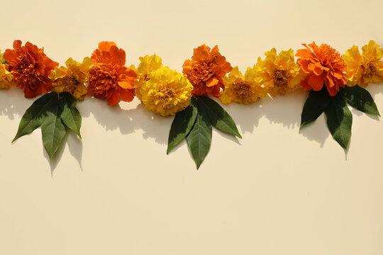 Traditional Indian marigold floral garland toran. Yellow orange zendu flowers, green leaves. Beige background. Festive culture symbol. Diwali, weddings, Dia de los Muertos Halloween celebrations decor