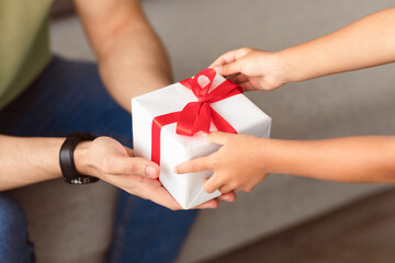 Celebrating Father's Day. Close up of little girl making surprise for her dad, holding and giving wrapped present box, greeting man with holiday. Above top high angle view, selective focus