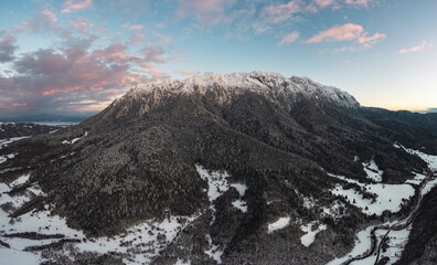 A beautiful mountain landscape shows Piatra Craiului covered in snow. The sky is colored with soft pastels from the sunset, painting the snowy peaks with a gentle glow
