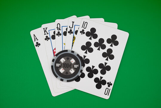 Royal flush in clubs with 100&euro; poker chip on green table, symbolizing ultimate poker hand, casino gambling, and high-stakes games.