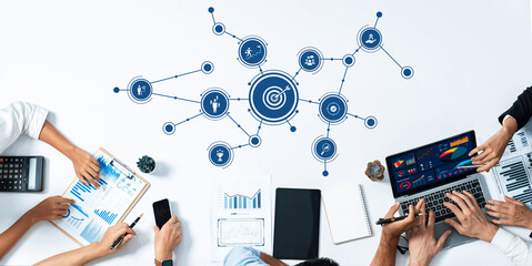 A diverse team of professionals is engaged in a collaborative meeting, analyzing data and discussing business strategies using digital tools and visual aids. Amity
