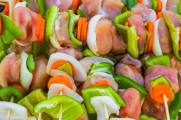 Raw chicken skewers with fresh vegetables like bell peppers, onions and carrots prepared for outdoor barbecue