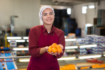 Smiling young female sorter working on citrus sorting line in agricultural produce processing factory, holding pile of ripe mandarins © JackF