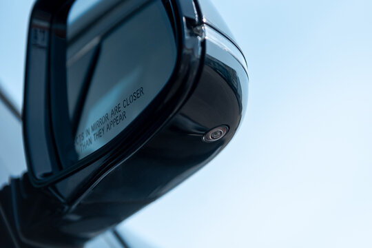 Car side view mirror with built in camera - part of 360 degrees surround view parking system cameras in a car. "objects in mirror are closer than they appear" written on car mirror.