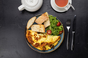 Healthy breakfast with omelet, ciabatta, salad and tea on dark stone background